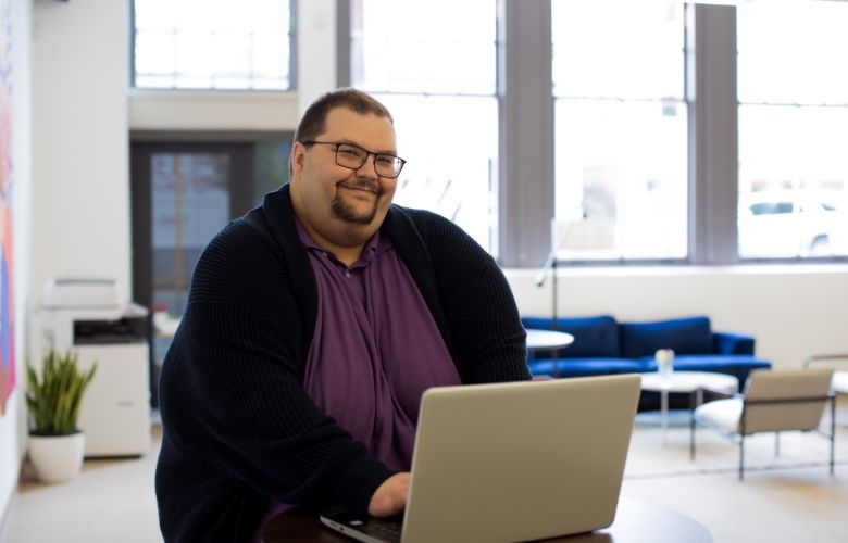 Smiling man seated and using a laptop 