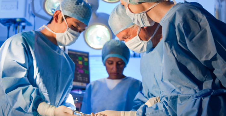 Four nurses and doctors wearing blue scrubs in operating theatre