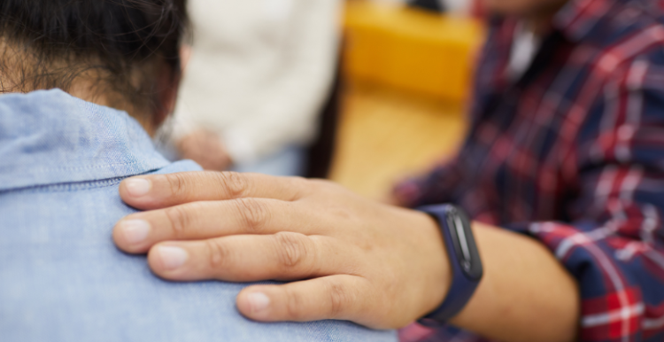 A person putting their hand on someones shoulder for support