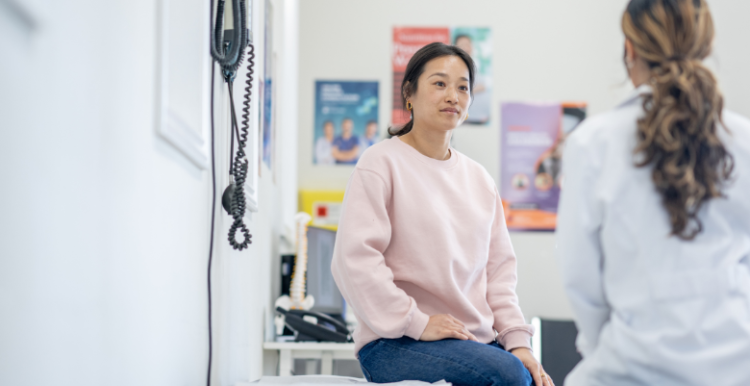 A lady sat on a bed at GP surgery talking to a doctor