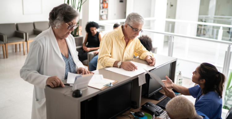 Patients at a waiting at a reception desk filling out paper work
