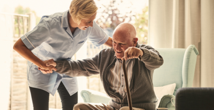 A carer supports an elderly man in a chair