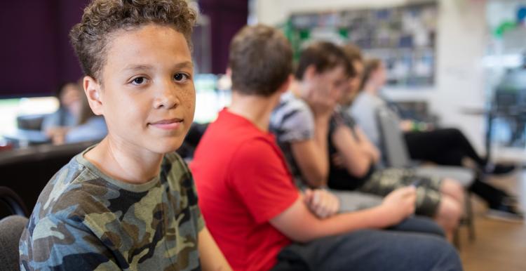 An image of a teenage boy sitting waiting with other children