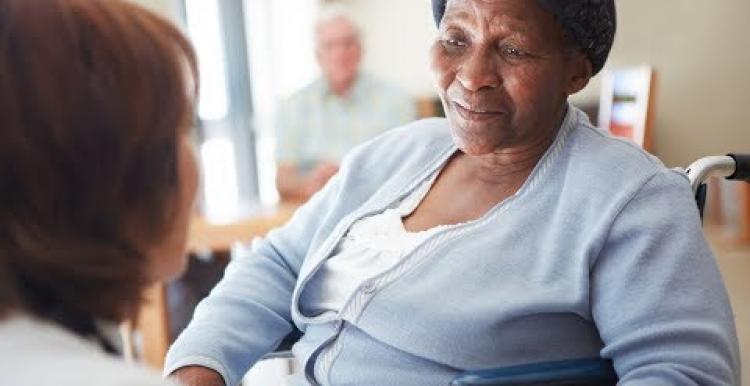 Black older woman in a nursing home being spoken to by a carer