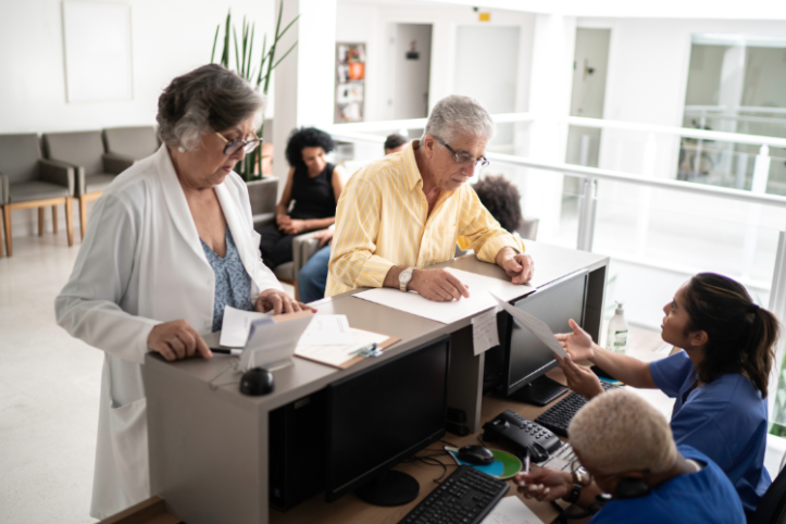 Patients at a waiting at a reception desk filling out paper work