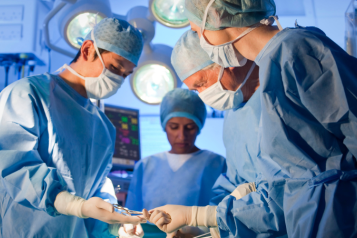 Four nurses and doctors wearing blue scrubs in operating theatre