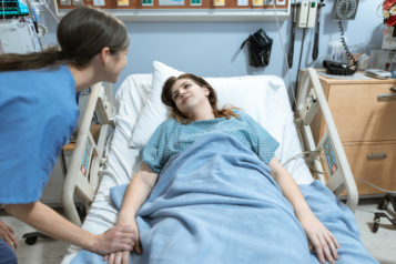 Patient lying in a hospital bed looking at a nurse.