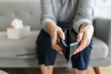 Person sat on a sofa holding out an empty wallet