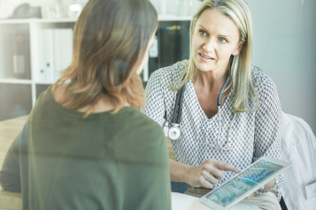 Image of a doctor talking to a patient and looking at a tablet screen
