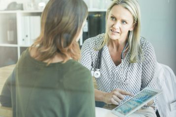 Image of a doctor talking to a patient and looking at a tablet screen 