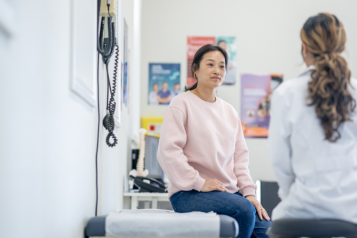 A lady sat on a bed at GP surgery talking to a doctor