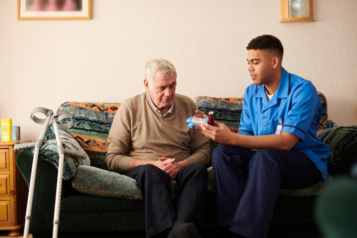 Elderly man receiving medication from a carer