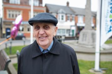 An older man wearing a hat standing out doors and smiling at the camera