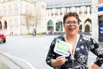 Healthwatch staff member holds an It Starts With You sign to promote giving views