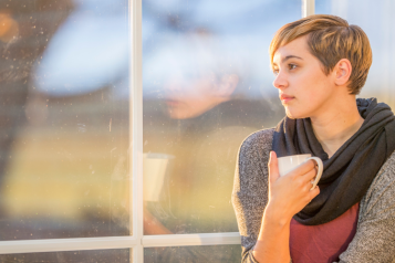 An image of a person holding a cup gazing out of a window
