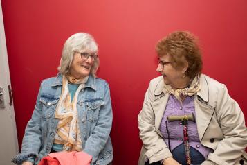 Two women sat down talking to each other, waiting for the bus