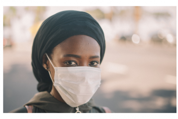 Young black woman staring into the camera lens. She is wearing a face mask.