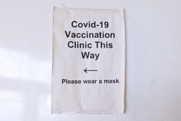 A paper sign with arrow which reads "Covid-19 vaccination clinic this way. Please wear a mask".