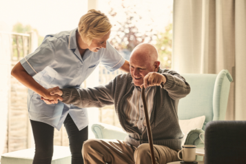 A carer supports an elderly man in a chair