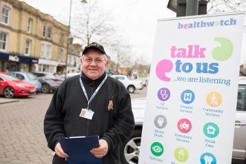 Healthwatch volunteer standing next to banner with a clipboard