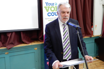 Picture of Stuart Linnell standing at a lectern in for of Healthwtch banner