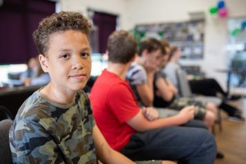 An image of a teenage boy sitting waiting with other children