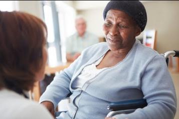 Black older woman in a nursing home being spoken to by a carer