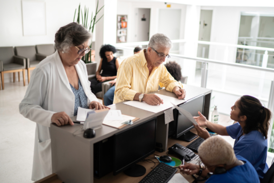 Patients at a waiting at a reception desk filling out paper work