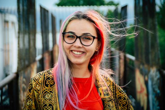 Young woman with colourful hair and glasses standing outside