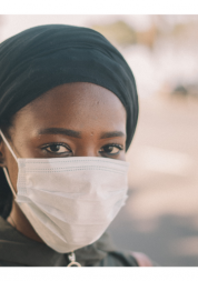 Young black woman staring into the camera lens. She is wearing a face mask.